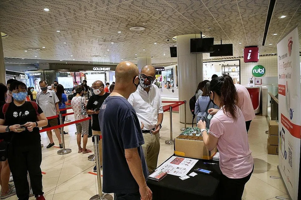 PENGAGIHAN DI KEJIRANAN: Dr Janil Puthucheary (kemeja putih) dilihat sedang menemui penduduk yang beratur untuk mendapatkan token TraceTogether di stesen pengagihan token itu di Bedok Mall semalam. - Foto BH oleh KELVIN LIM