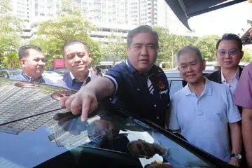 Menteri Pengangkutan Malaysia, Encik Anthony Loke (tiga dari kiri), menunjukkan pelekat Permit Masuk Kenderaan (VEP) yang siap dipasang ketika lawatan kerja ke Pusat Pungutan VEP bagi meninjau persiapan pelaksanaan penguatkuasaan VEP mulai 1 Oktober 2024.