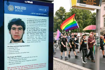 Orang ramai menyertai perarakan memperingati mangsa serangan rempuhan kenderaan berhampiran laluan perarakan Christopher Street Day (CSD) di Berlin, Jerman, pada 26 Julai 2026. Paparan elektronik di laluan itu memaparkan rayuan polis bagi mendapatkan maklumat mengenai suspek, Abdul Ballout, yang dipercayai mempunyai kaitan dengan kumpulan Islamis. Serangan itu mengorbankan seorang wanita dan mencederakan 29 lagi, manakala pihak berkuasa menyiasatnya sebagai serangan pengganas