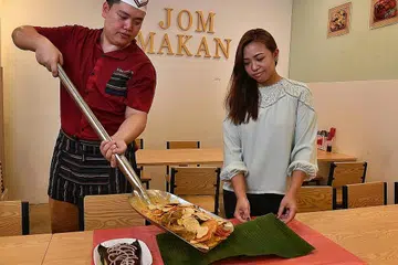 MAKANAN LAUT DALAM PENYODOK: Cef Desmond Lim semasa menghidangkan makanan laut berperisa telur asin di atas daun pisang yang dipegang Cik Norfaraha Azman, menggunakan penyodok sepanjang 1.12 meter di restoran Jom Makan BBQ Seafood. - Foto BM oleh CHONG JUN LIANG