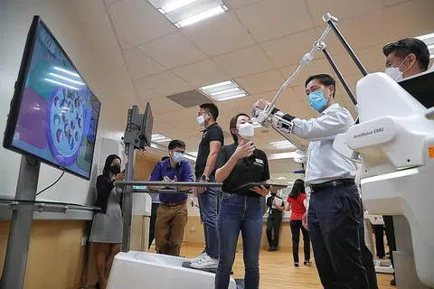 CUBA ROBOTIK: Menteri Kesihatan, Encik Ong Ye Kung (dua dari kanan) sedang mencuba ArmMotus EMU, iaitu robot yang direka khas untuk pemulihan semula bahagian anggota tubuh atas dalam lawatannya ke Cart semalam.- Foto-foto BH oleh KEVIN LIM