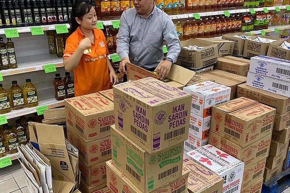 HABIS DIBELI: Encik Ronnie Faizal Tan dengan kakitangannya yang sedang meletakkan makanan dalam tin di rak-rak selepas habis dibeli pelanggan. Menurut beliau, pasar rayanya penuh sesak sejak Jumaat lalu. - Foto ihsan RONNIE FAIZAL TAN