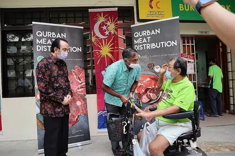 BAWA KECERIAAN: Encik Murali (tengah) bersama Presiden Jamiyah Singapura, Datuk Dr Mohd Hasbi Abu Bakar (kiri), memberi daging korban kepada seorang penduduk Bukit Batok. - Foto JAMIYAH SINGAPURA