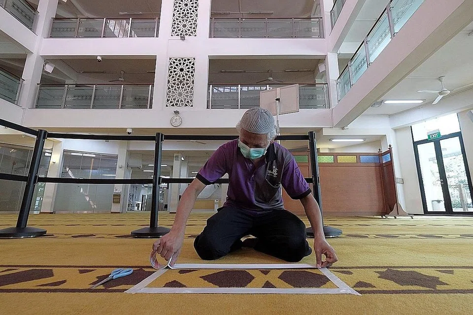 PERSIAPAN BERJALAN LANCAR: Encik Mohd Maksod Nabi Ahamad, ketua jabatan Aset dan Kemudahan di Masjid Mujahidin melekatkan pelekat putih di permaidani dewan solat. Jemaah individu diminta berdiri di dalam kotak ini semasa menunaikan ibadah. Jemaah yang pergi ke masjid dengan seisi keluarga pula diminta menunaikan solat di ruang yang dipagari papan, yang boleh dilihat di belakang Encik Maksod. - Foto-foto BH oleh GAVIN FOO