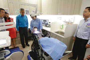 POLIKLINIK DIPERTINGKAT: Perdana Menteri Lee Hsien Loong (tiga dari kiri) yang ditemani (dari kiri) Menteri Negara Kanan (Kesihatan merangkap Pengangkutan), Dr Lam Pin Min; CEO NHGP Profesor Madya Chong Phui-Nah; serta Pengarah Perkhidmatan Dental NHGP Dr Kenneth Low (kanan) memerhatikan penggunaan penyondong kereta roda di Poliklinik Ang Mo Kio yang dipertingkat awal tahun ini. - Foto BH oleh KEVIN LIM