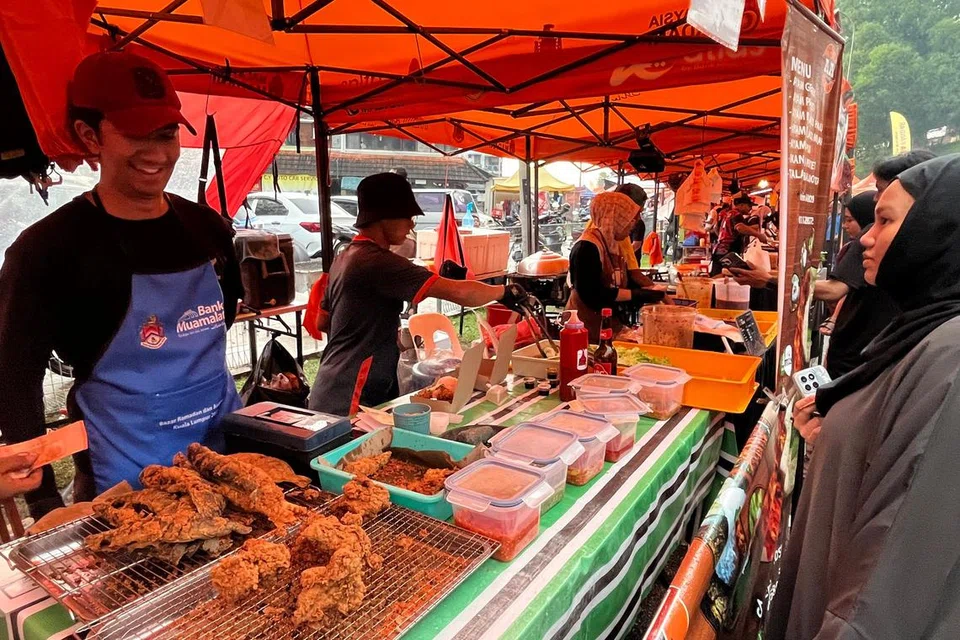 Peniaga nasi ayam penyet di bazar Ramadan Wangsa Maju, Encik Mohd Hafiz Tukiran, 31 tahun (kiri) melayan pelanggan di gerainya.