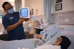 Jururawat, Encik Muhammad Hafizuddin, membantu pesakit, Cik Mislina Timat, menggunakan tablet di sisi katil pesakit yang membolehkan pesakit mendapat mengakses bahan pendidikan kesihatan, rekod kesihatan, permainan mahupun YouTube di hospital akut kampus Woodlands Health pada 3 Julai.