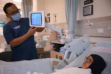 Jururawat, Encik Muhammad Hafizuddin, membantu pesakit, Cik Mislina Timat, menggunakan tablet di sisi katil pesakit yang membolehkan pesakit mendapat mengakses bahan pendidikan kesihatan, rekod kesihatan, permainan mahupun YouTube di hospital akut kampus Woodlands Health pada 3 Julai.