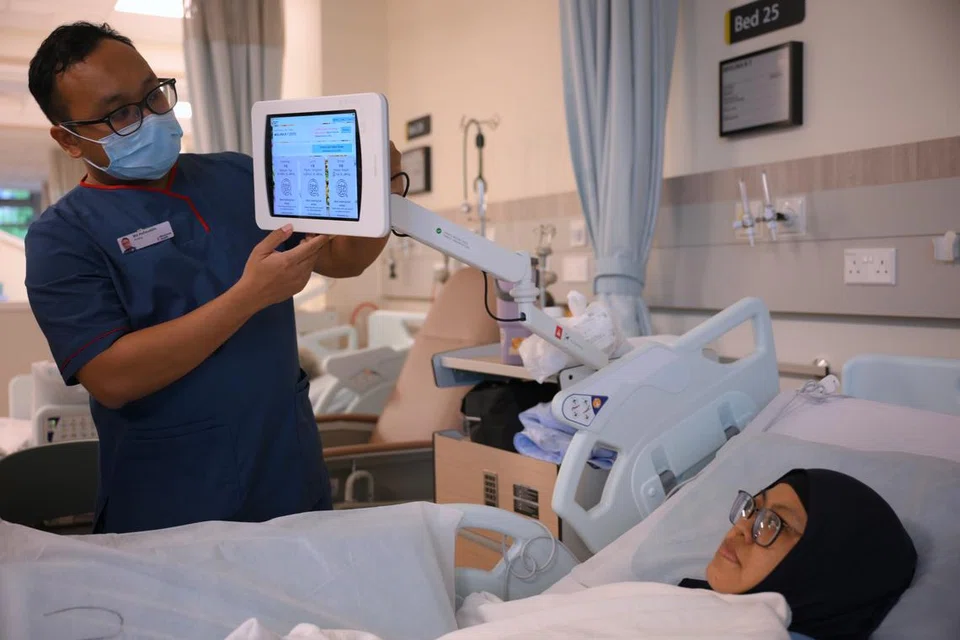 Jururawat, Encik Muhammad Hafizuddin, membantu pesakit, Cik Mislina Timat, menggunakan tablet di sisi katil pesakit yang membolehkan pesakit mendapat mengakses bahan pendidikan kesihatan, rekod kesihatan, permainan mahupun YouTube di hospital akut kampus Woodlands Health pada 3 Julai.