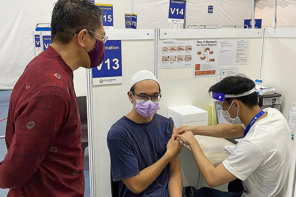 GEMBIRA DAPAT VAKSIN: Dr Maliki (kiri) menyaksikan Muhammad Faeiz, pelajar Madrasah Aljunied Al-Islamiah yang menerima vaksinasi di salah sebuah pusat vaksinasi di Our Tampines Hub. - Foto ERWIN YUHANIS YUNAHAR
