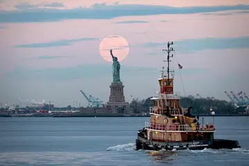 KEADAAN BERUBAH: Amerika Syarikat kini menghadapi kemelesetan ekonomi selepas ia berkembang selama 128 bulan sebelum berakhir pada Februari lalu. Kelihatan bulan penuh pada Mei lalu, dikenali sebagai Bulan 'Bunga Mengambang' yang berlaku pada 7 Mei lalu dan dapat dilihat dari pelabuhan New York dengan Patung Liberty seakan mencapai bulan tersebut.