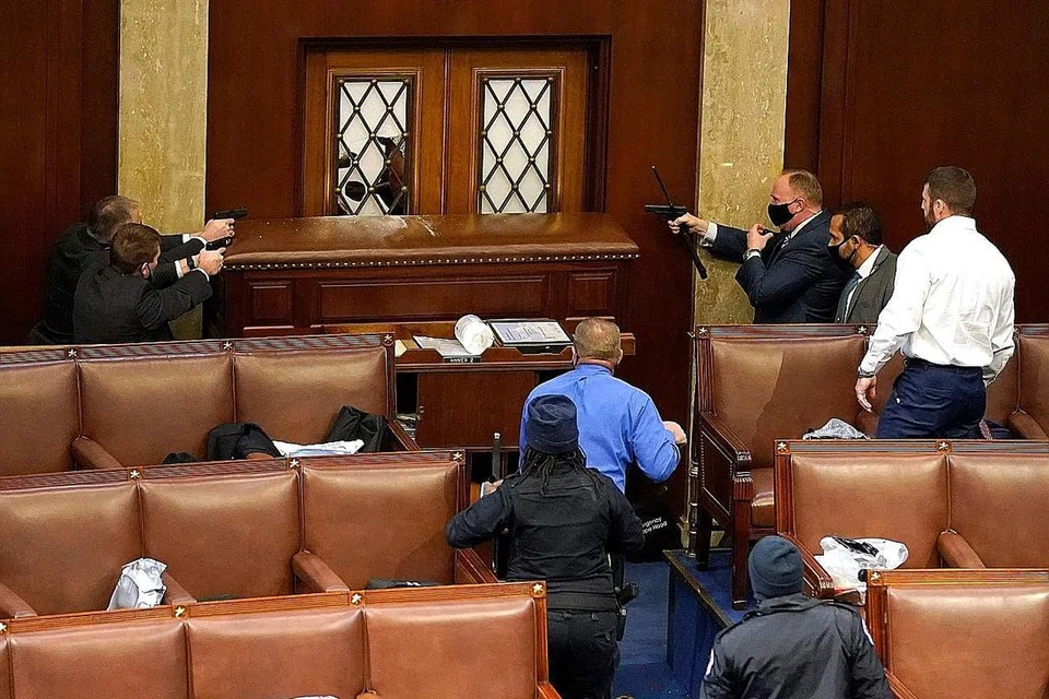 HUNUS SENJATA: Pegawai polis mengacu pistol ke arah pintu yang telah dirosakkan perusuh yang telah menyerbu masuk Bangunan Capitol semasa sesi bersama Dewan Kongres sedang berlangsung kelmarin. 