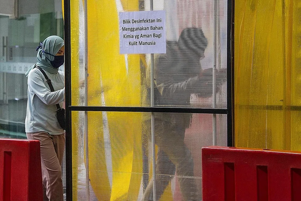 'BERSIHKAN' DIRI: Orang ramai melalui ruang semburan nyah kuman sebelum memasuki sebuah pusat beli-belah di Surabaya, dalam usaha mencegah penularan Covid-19. - Foto AFP 