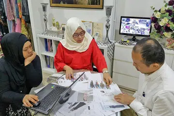 NASIHAT KE JEPUN: Cik Lynn (tengah) dan pekerjanya, Cik Siti Raudhah Au Talib (kiri), sedang berbincang dengan konsultan dari Jepun, Encik Yoko San, yang sering ulang-alik ke Singapura, tentang saranan pereka fesyen dari Jepun. - Foto TUDUNGKU
