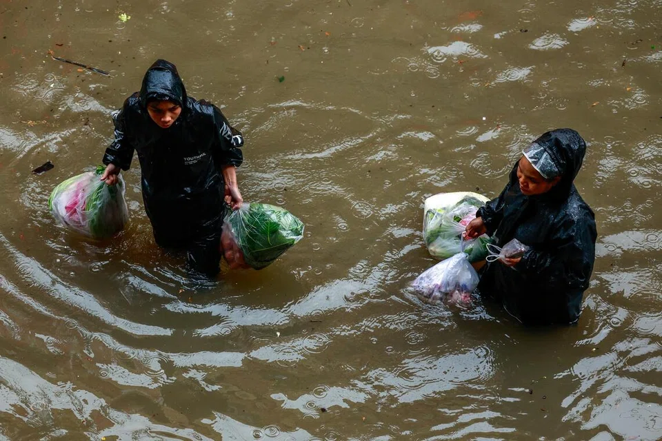 Penduduk membawa barangan runcit sambil meredah jalan yang dinaiki air ketika hujan lebat di Bangkok, Thailand, pada 26 September.
