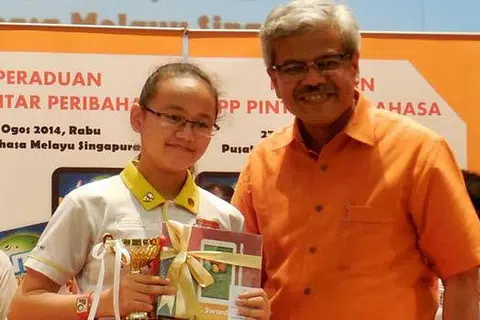 DENGAN HADIAH KEMENANGAN: Nurul Janna Muhammad Muhiddin bergambar bersama Encik Mohd Noh Daipi selepas menerima hadiah kemenangan dalam peraduan yang dianjurkan Pusat Bahasa Melayu Singapura pada Rabu lalu. - Foto MOHD RAMAN DAUD