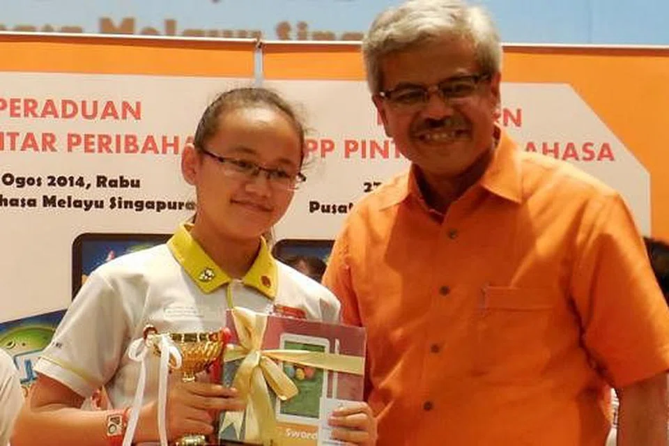 DENGAN HADIAH KEMENANGAN: Nurul Janna Muhammad Muhiddin bergambar bersama Encik Mohd Noh Daipi selepas menerima hadiah kemenangan dalam peraduan yang dianjurkan Pusat Bahasa Melayu Singapura pada Rabu lalu. - Foto MOHD RAMAN DAUD