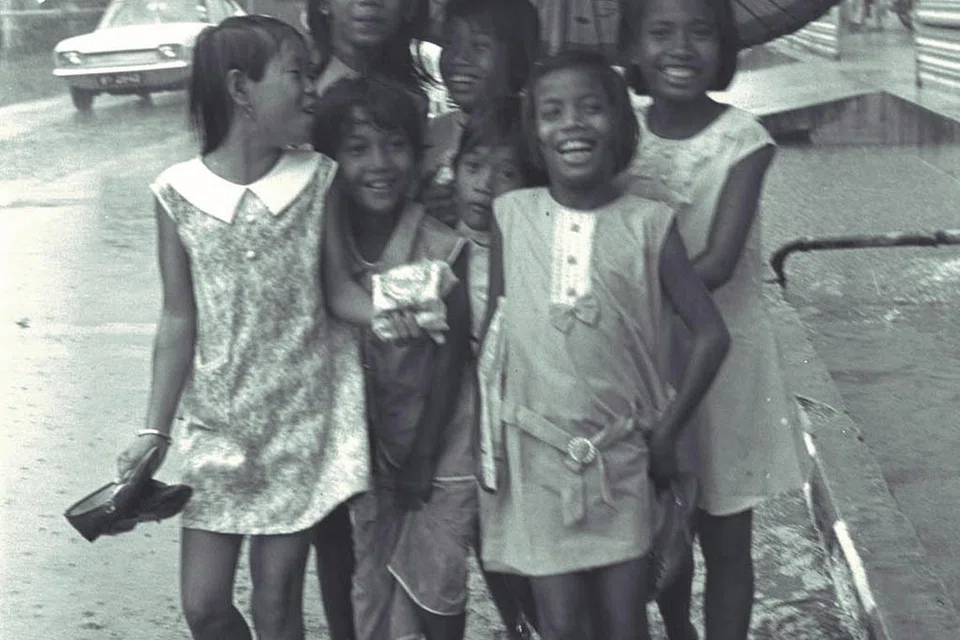 Sekumpulan kanak-kanak perempuan berkongsi payung untuk meredah hujan supaya mereka boleh meneruskan kegiatan jalan raya, dalam gambar yang diambil pada Disember 1970 ini. Hari Raya pada tahun itu jatuh pada musim tengkujuh. 