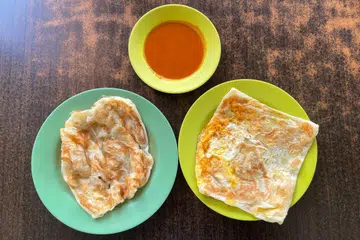 Roti perata kosong (kiri) dan roti perata telur (kanan) bersama kuah kari ikan yang masam dan pedas. 