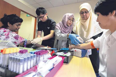 TUNJUK CARA: Cik Nafisah (tengah) menunjukkan cara bagaimana beliau membimbing kakitangannya melakukan flebotomi. Mereka ialah (dari kiri), Cik Sarada Devi, Encik Teo Rong Jie, Cik Muslina Mohd Salleh dan Cik Margaret Goh. - Foto ZAINAL YAHYA