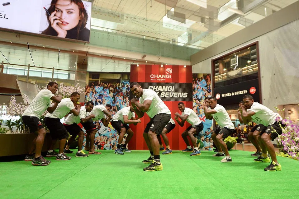 TARIAN SAHUT CABARAN: Pemain Fiji, yang merupakan juara bertahan dalam Kejohanan Ragbi Tujuh Sepasuk Dunia ini, melakukan tarian 'Cibi' (disebut 'Thimbi') yang biasa dilakukan sebelum perlawanan semasa membuat penampilan khas di Terminal 3 Lapangan Terbang Changi semalam. Mereka turut menemui peminat yang hadir dalam acara yang dianjurkan bersama Changi Airport Group (CAG) dan Fiji Airways. - Foto CAG
