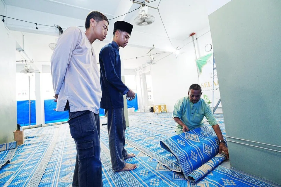 SEMANGAT KERJASAMA: Encik Mustaffa (kanan) bersama Encik Aqid Wahab (kiri) dan Encik Aqinan bergotong-royong membentang dan menyusun rapi tikar biru di kolong Blok 116 Simei Street 1 pada 14 Februari.