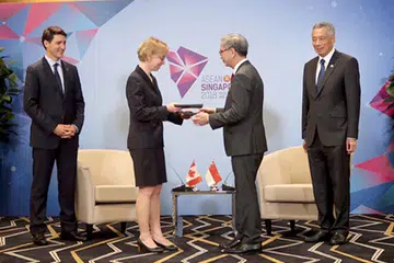 PERKUKUH KESELAMATAN SIBER: Encik Koh (kanan) bertukar-tukar MOU ditandatangani dengan Cik McDonald, sambil diperhatikan oleh PM Lee dan PM Trudeau. - Foto CSA