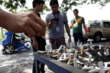LARANGAN SEDANG DITIMBANG: Seorang perokok meletakkan puntung rokok di tempat membuang rokok dekat jalan raya di bandar Las Pinas, Manila, baru-baru ini, sedang pemerintah negara itu menimbangkan langkah melarang merokok di tempat awam. - Foto REUTERS