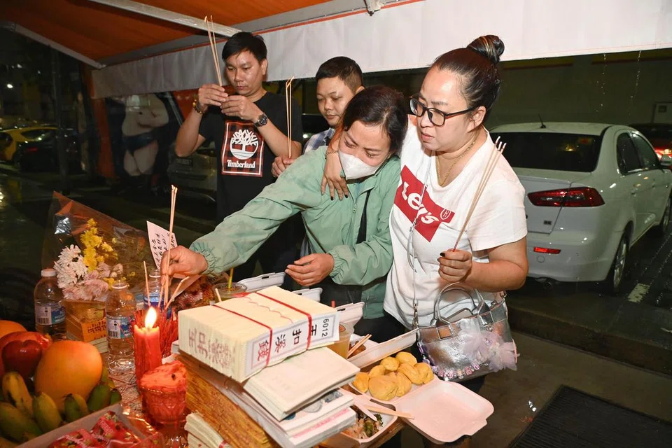 Kakak mangsa (tiga dari kiri) tidak dapat menahan sebak dan dipeluk oleh rakannya di altar sementara yang didirikan di belakang kedai untuk mengenang mangsa. 