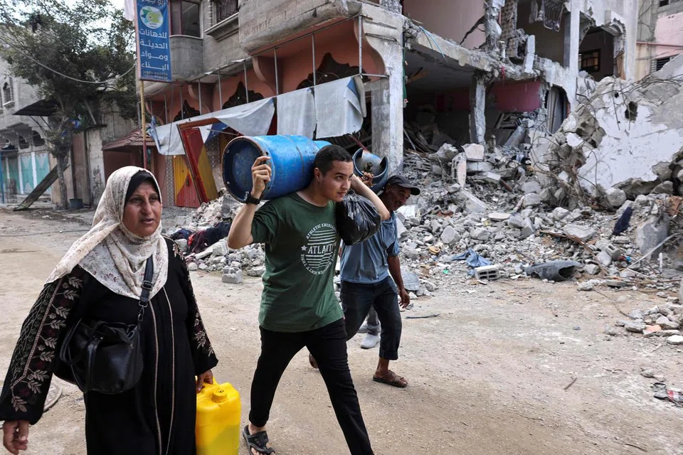 TERUSKAN KEHIDUPAN: Penduduk Gaza kelihatan mengangkat tong gas sedang wilayah itu menghadapi kekurangan bekalan minyak.
