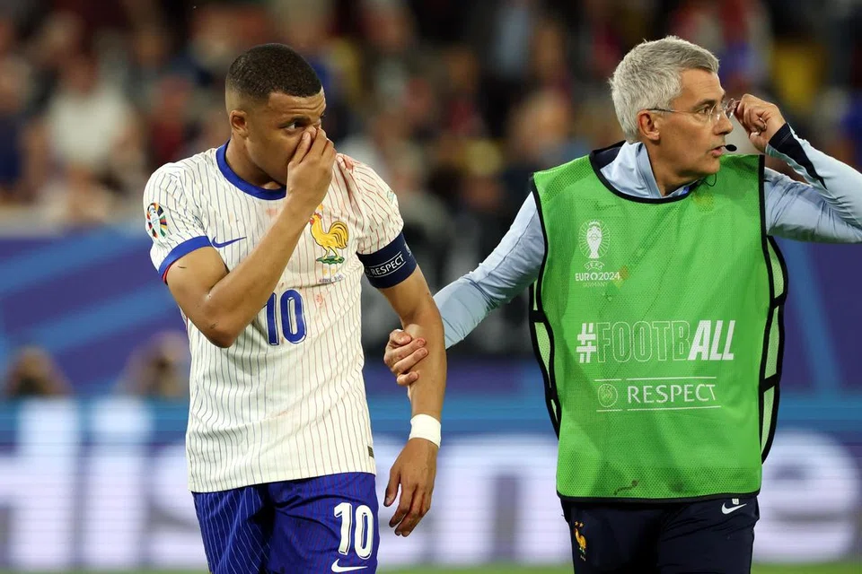 Kapten Perancis, Kylian Mbappe (kiri), memegang hidungnya sambil dibawa keluar padang untuk menerima rawatan daripada kakitangan perubatan.