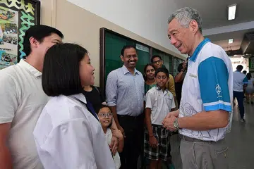 PENERIMA DERMASISWA: PM Lee berbual mesra dengan Samantha Ong (dua dari kiri) dari Sekolah Rendah Townsville dan Rivash Dhayalan (tujuh dari kiri) dari Sekolah Rendah Teck Ghee dan keluarga masing-masing. - Foto BH oleh NG SOR LUAN