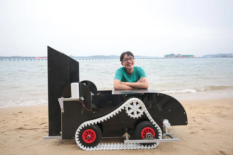 Pelajar SUTD, Encik Vincent, mengambil gambar di hadapan robotnya yang membantu mengutip sampah di pantai.