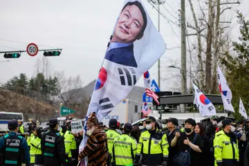 Polis berdiri di antara penyokong pro-Yoon Suk Yeol (gambar beliau tertera pada bendera) di lokasi berhampiran perhimpunan yang dianjurkan oleh ahli Liga Petani Korea (tidak kelihatan dalam gambar), kebanyakannya petani dari wilayah luar bandar, yang menyertai protes menentang Presiden Korea Selatan yang telah dipecat, Yoon Suk Yeol, di Seoul pada 25 Mac 2025.