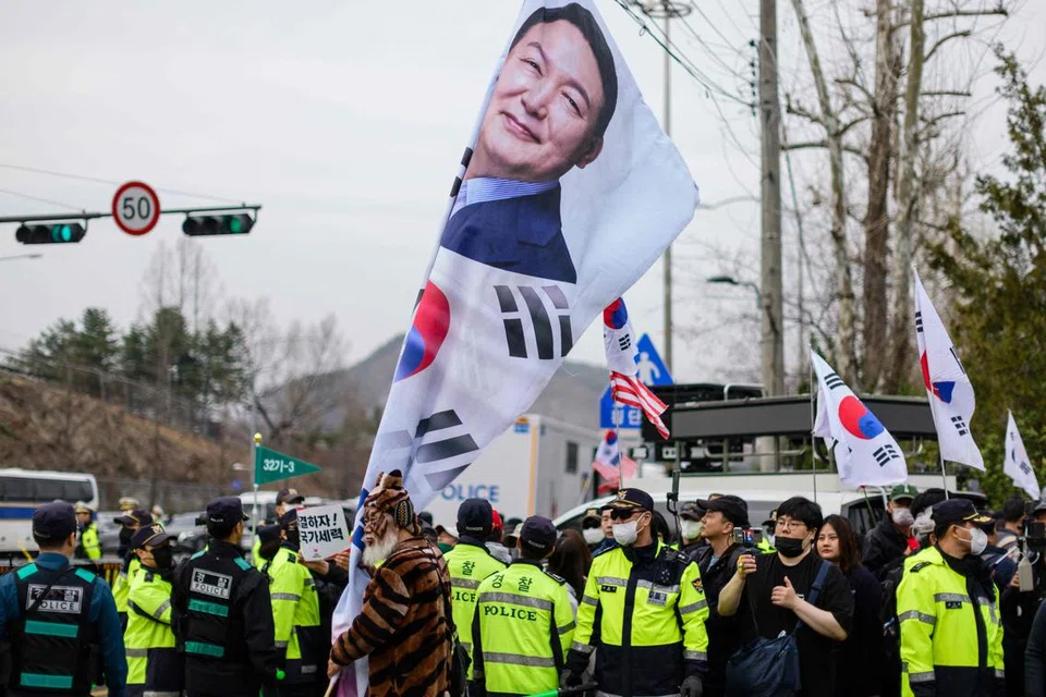 Polis berdiri di antara penyokong pro-Yoon Suk Yeol (gambar beliau tertera pada bendera) di lokasi berhampiran perhimpunan yang dianjurkan oleh ahli Liga Petani Korea (tidak kelihatan dalam gambar), kebanyakannya petani dari wilayah luar bandar, yang menyertai protes menentang Presiden Korea Selatan yang telah dipecat, Yoon Suk Yeol, di Seoul pada 25 Mac 2025.
