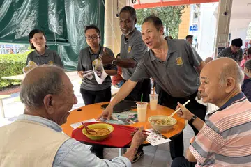Setiausaha Agung Parti Besatu Singapura (SUP),  Encik Andy Zhu (berdiri, kanan), bersama pengerusi SUP, Encik Ridhuan Chandran (berdiri, dua dari kanan) berbual dengan penduduk di Pasar dan Pusat Makanan Chong Boon pada 6 April.