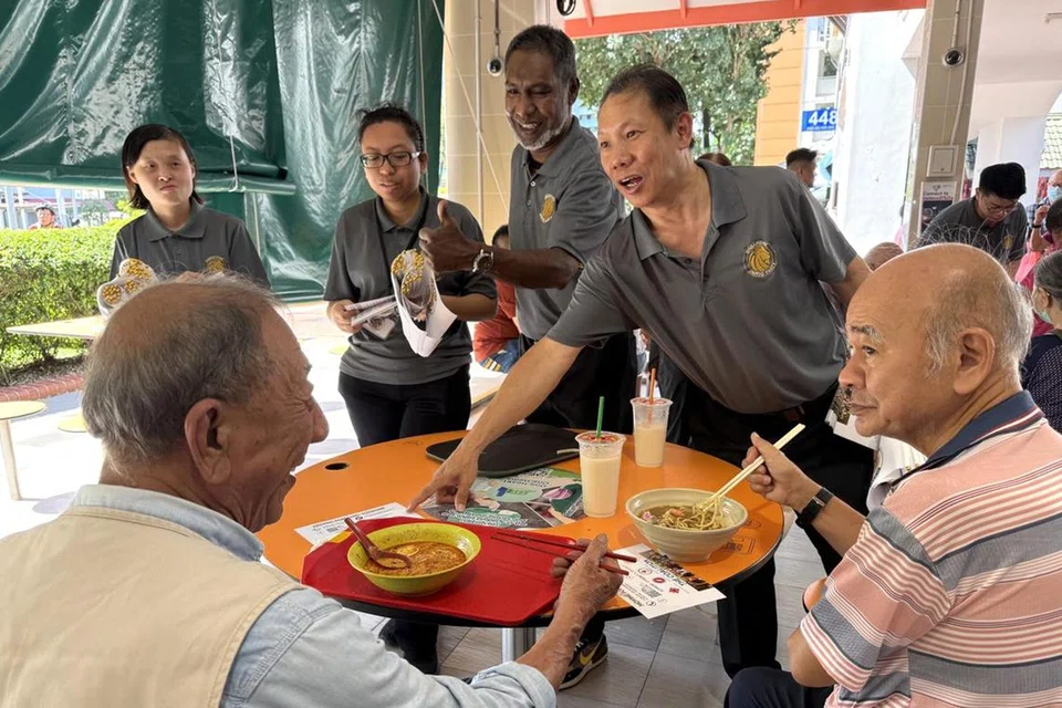 Setiausaha Agung Parti Besatu Singapura (SUP),  Encik Andy Zhu (berdiri, kanan), bersama pengerusi SUP, Encik Ridhuan Chandran (berdiri, dua dari kanan) berbual dengan penduduk di Pasar dan Pusat Makanan Chong Boon pada 6 April.