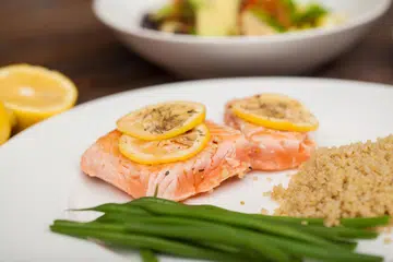 Ikan salmon dihidangkan dengan sedikit lemon dan herba bersebelahan dengan beberapa kuinoa dan kacang hijau