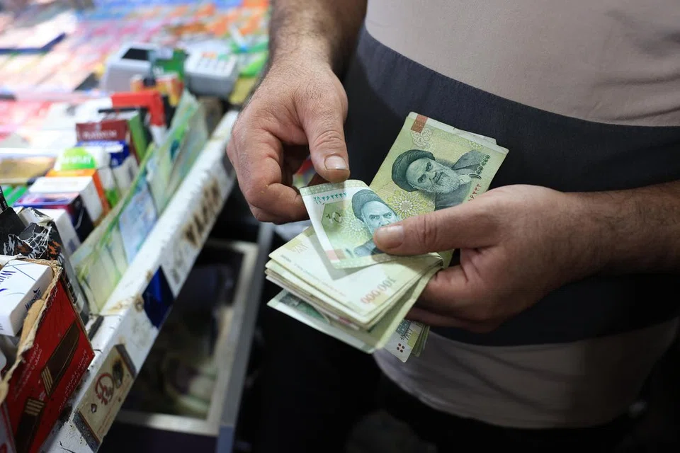 Seorang peniaga Iran mengira wang kertas seratus ribu rial di kiosnya di Tehran, Iran, 4 Ogos 2025. Jawatankuasa Parlimen Iran pada 3 Ogos telah meluluskan rancangan terdahulu untuk membuang empat sifar daripada mata wang negara yang terus merosot nilainya, bagi memudahkan urusan perdagangan dan transaksi kewangan di tengah krisis ekonomi.