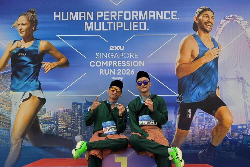 BERBAJU MELAYU: Encik Muhammad Dani Mirza Ahmad Affandi (kiri) dan Encik Muhamad Nurirsyad Azman bergambar di podium setelah selesai berlari dalam acara separuh maraton sejauh 21.1 kilometer, 2XU Compression Run 2026, dengan berbaju Melayu lengkap dengan samping dan songkok.