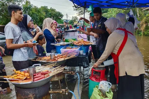 JUALAN LARIS: Peniaga sosej talam, Cik Saida Fauzi, 55 tahun (kanan), yang juga seorang ibu tunggal, meraih pendapatan berganda setiap kali musim tengkujuh melalui jualan makanan di Kampung Pohon Tanjong di Pasir Mas, Kelantan.