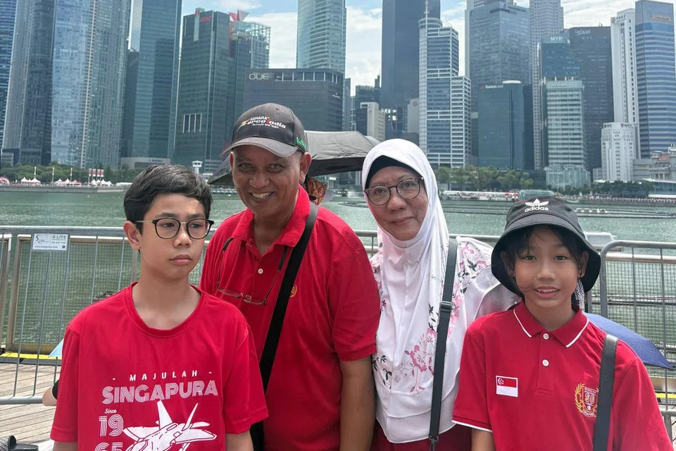 Cik Safurah Ismail bersama suaminya, Encik Mohammed Ali gembira dapat membawa cucu-cucu mereka, Sheh Muhammad Shahrezza Muhammad Fuad (kiri) dan Wan Nur Shahzana Muhammad Fuad (kanan) keluar melihat terbang lalu jet pejuang di kawasan sekitar Marina Bay Sands (MBS).
