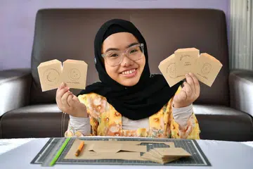SAMPUL 'HIJAU': Cik Yulianna menghasilkan sampul duit Raya menggunakan kertas yang dikitar semula bagi mengurangkan pembaziran. - Foto BH oleh LIM YAOHUI
