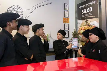 SOKONGAN DIPERLUAS: Pemilik kafe fusion Eatz 19, Cik Shakila Mohd Sham (dua dari kanan) telah memanfaatkan Program Go Digital SME kelolaan Penguasa Pembangunan Media Infokom (IMDA). - Foto Fail