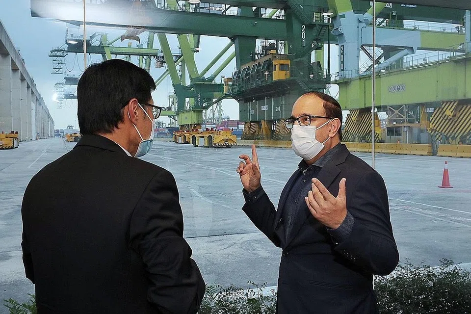TINJAU KEMUDAHAN: Menteri Perhubungan dan Penerangan S Iswaran (kanan) berbual dengan Ketua Pembangunan Tuas Encik Nelson Quek semasa demonstrasi Kenderaan Berpandu Automatik (AGV), yang menggerakkan kontena pengiriman di sekitar pelabuhan di Terminal Pasir Panjang. - Foto BH oleh GAVIN FOO