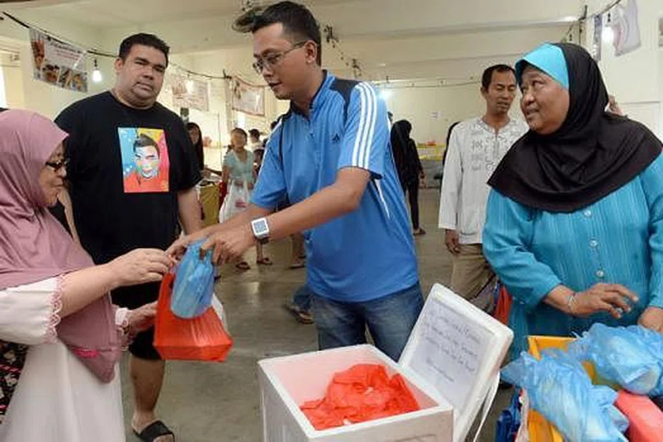 MEMERIAHKAN RAMADAN: Encik Shafiee (berkaca mata) mengedarkan sebungkus nasi goreng dan air katira kepada orang ramai di gerai bazar Ramadan Tampines ibunya, Cik Salmah Ismail (berbaju biru), Ahad lalu. - Foto TAUFIK A. KADER