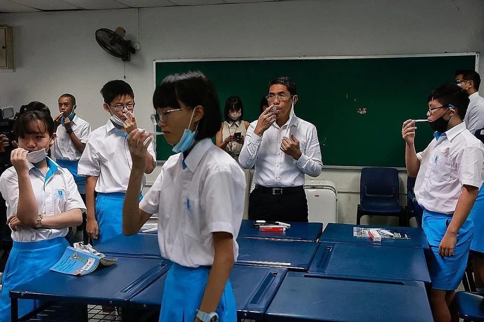 RUTIN HARIAN BARU: Dr Mohamad Maliki Osman menyertai pelajar Menengah Satu Sekolah Hai Sing Catholic mengambil suhu badan mereka dalam bilik darjah semalam. Pengambilan suhu badan merupakan rutin harian bagi pelajar, sebahagian langkah pengurusan selamat yang ditetapkan. - Foto BH oleh KEVIN LIM