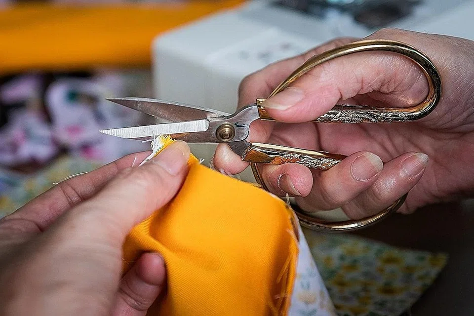 HASIL YANG KEMAS: Seorang sukarelawan menggunting benang-benang di hujung kain untuk memastikan hasil selimut yang dijahit kemas dan rapi. - Foto BH oleh GAVIN FOO