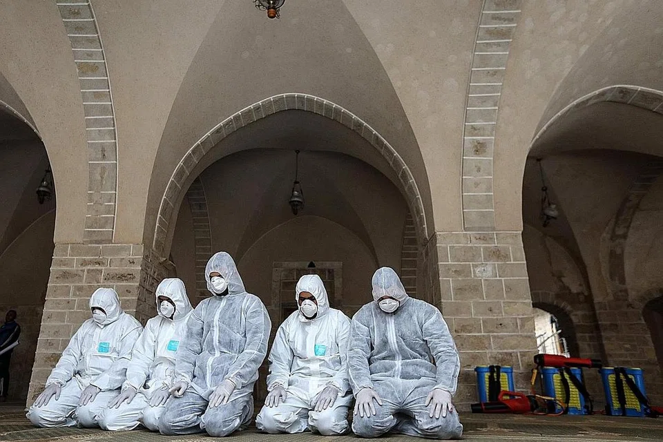 BERSIHKAN MASJID: Pekerja Palestin dengan pakaian perlidungan menyahjangkit tembok di dalam Masjid Al-Omari sebagai langkah pencegahan mengekang penularan Covid-19. (gambar atas) Para pekerja yang sama solat sebentar selepas menjalankan kerja pembersihan. - Foto AFP