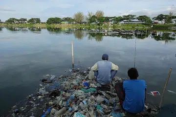 PENCEMARAN TERUK: Dua lelaki yang memancing kelihatan duduk di atas timbunan sampah plastik di sebuah kolam ikan di Aceh, Indonesia. - Foto AFP